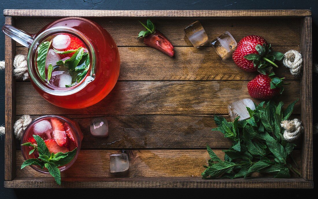 Homemade strawberry lemonade with mint and ice, served with fresh berries over wooden tray surface