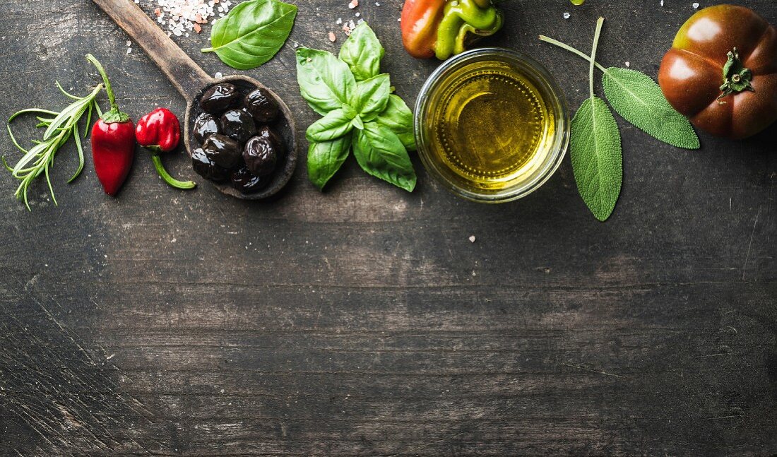 Schwarze Oliven, frisches Basilikum, Salbei, Rosmarin, Tomate, Paprika und Öl auf Holzuntergrund