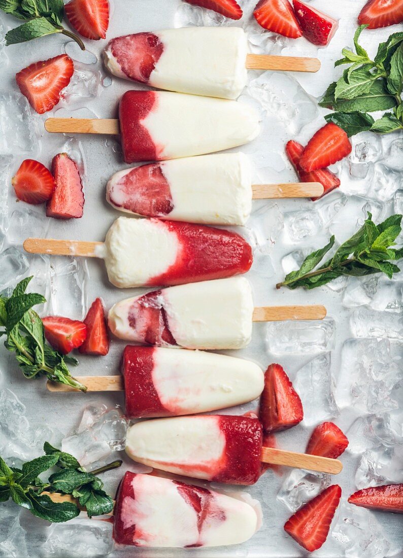 Strawberry yogurt ice cream popsicles with mint over steel tray background