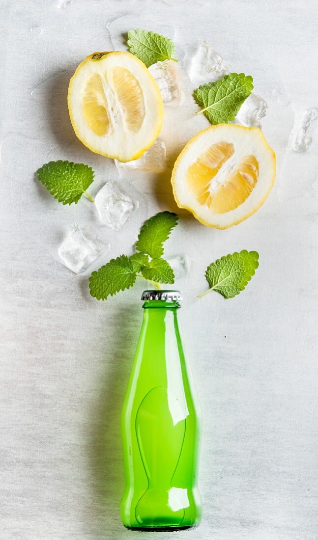 Green lemonade bottle with ingredients: lemons, mint and ice cubes