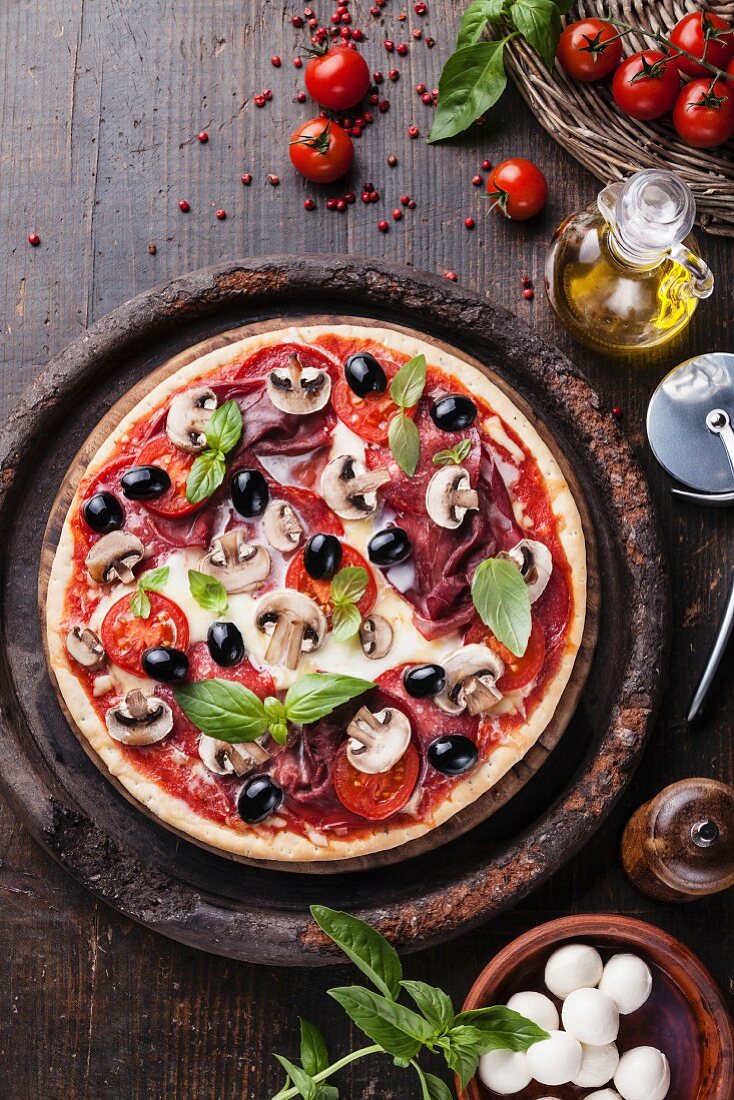 Pizza mit Salami, Pilzen und Oliven auf Holztisch
