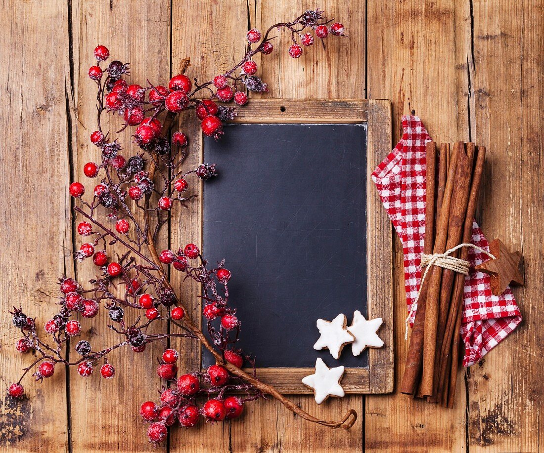 Vintage Christmas background with chalk board, branch with red berries, Xmas cookies and cinnamon sticks