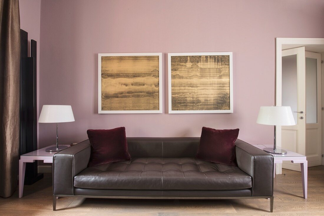 Red velvet scatter cushions on dark leather couch below two pictures on wall