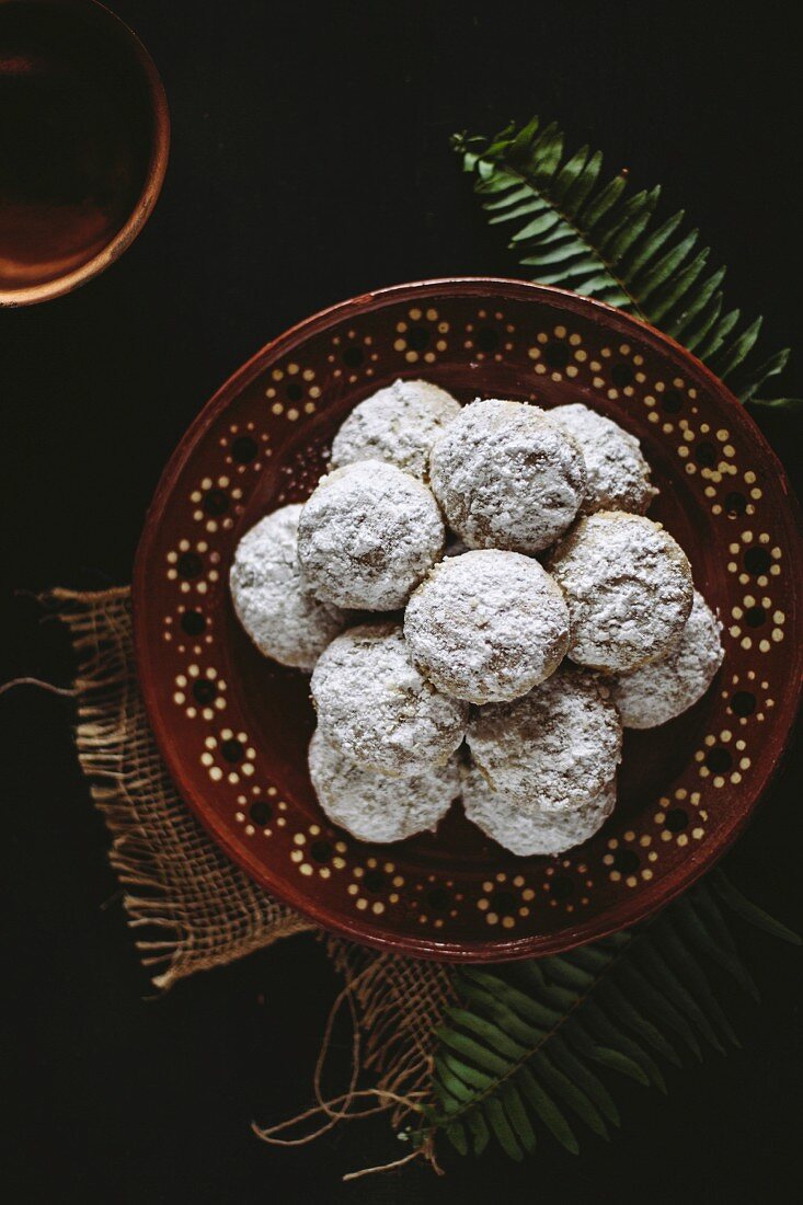 Mexican Wedding Cookies displayed on a traditional Mexican pottery plate on a dark background