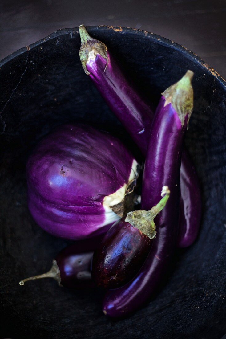 Different eggplants in a rustic bowl
