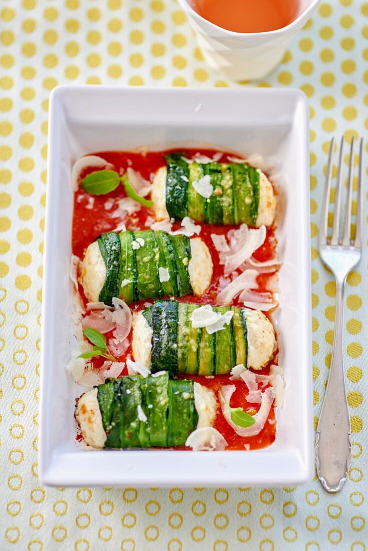 Zucchini rolls with fresh cheese filling on tomato sauce