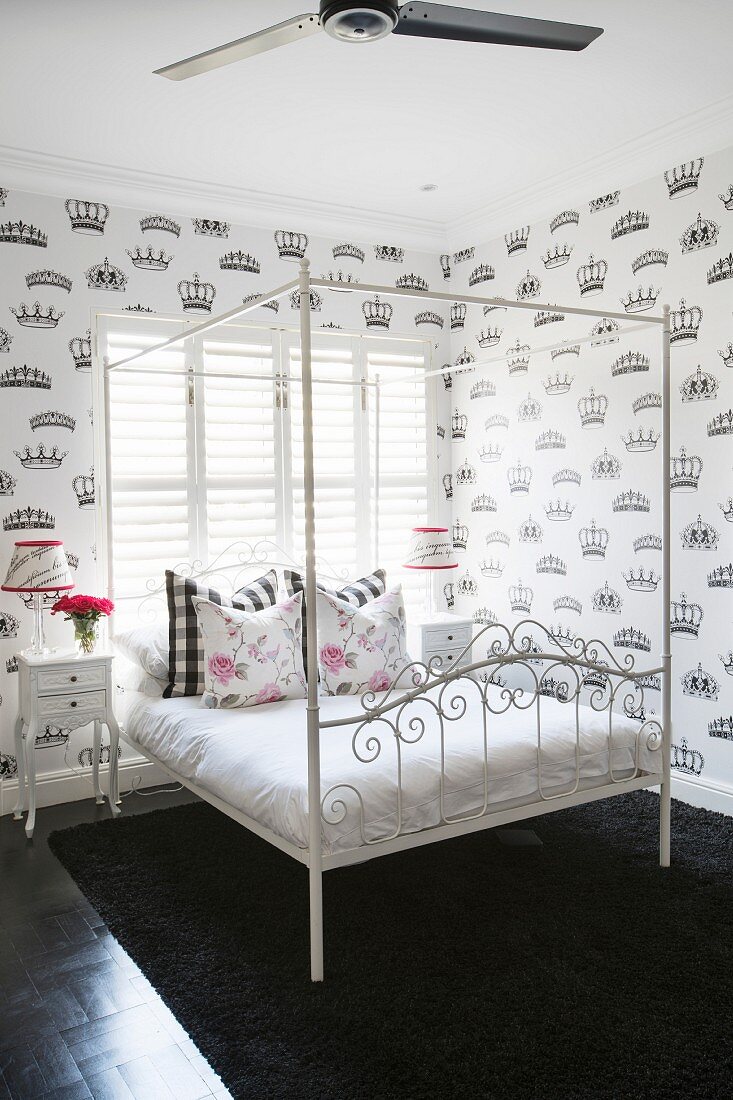 Four-poster bed with ornate frame and wallpaper with pattern of crowns