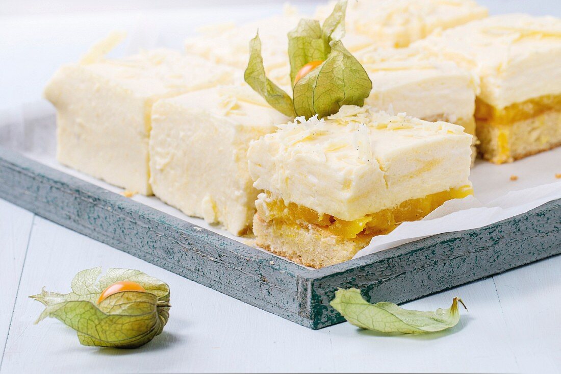 Homemade sliced cake with creamy mousse and tropical fruits mango and physalis served in wooden tray