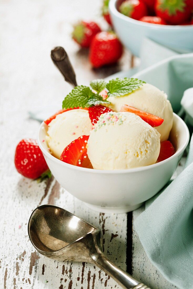 Vanilleeis mit frischen Erdbeeren in weissen Tassen auf Holzuntergrund