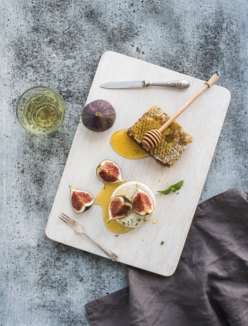 Camembert cheese with fresh figs, honeycomb and glass of white wine on serving board
