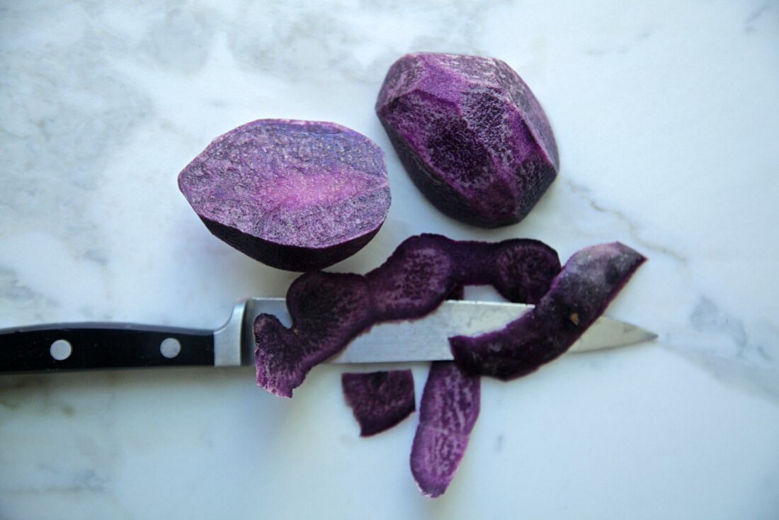 Purple potatoes, cut and peeled with knife on a white marble background