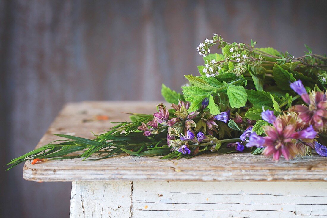 Assortment of fresh herbs mint, oregano, thym, blooming sage over old wooden background