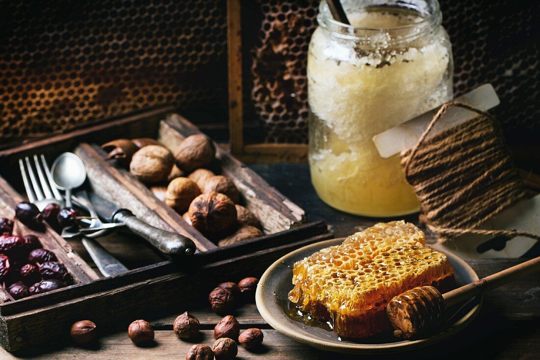 Frische Honigwabe, Glas mit altem Honig und verschiedene Nüsse auf altem Holztisch