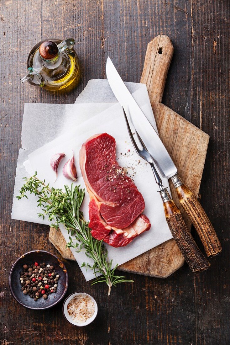 Raw fresh meat Ribeye steak entrecote and seasonings on cutting board on dark wooden background