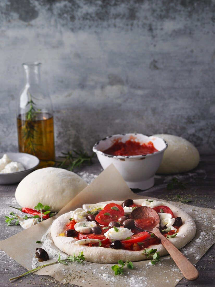 An unbaked pizza with tomato, black olives and mozzarella