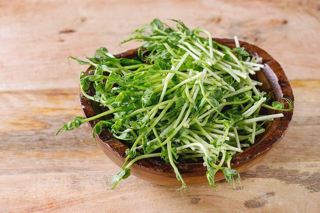 Wooden Bowl of pea sprouts over textured wooden background