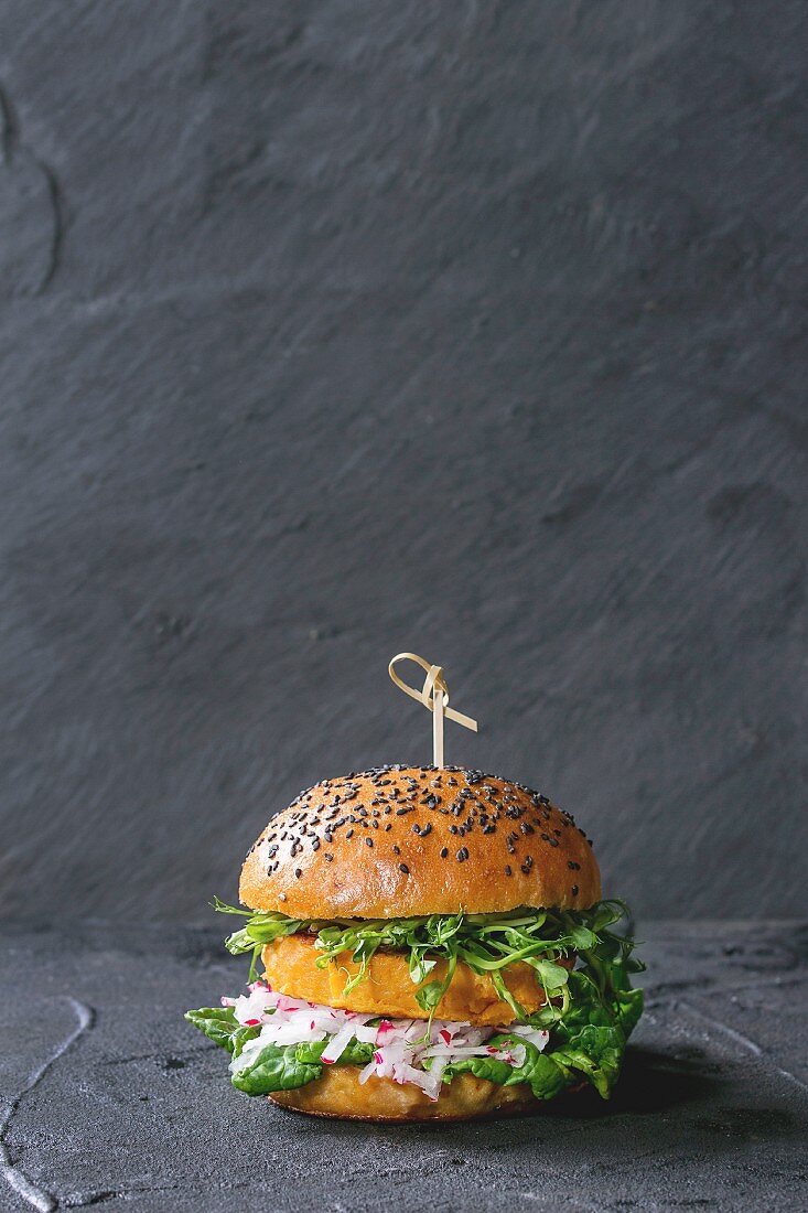 Selbst gemachter Süsskartoffel-Burger mit frischem Rettich und Erbsensprossen vor schwarzem Hintergrund