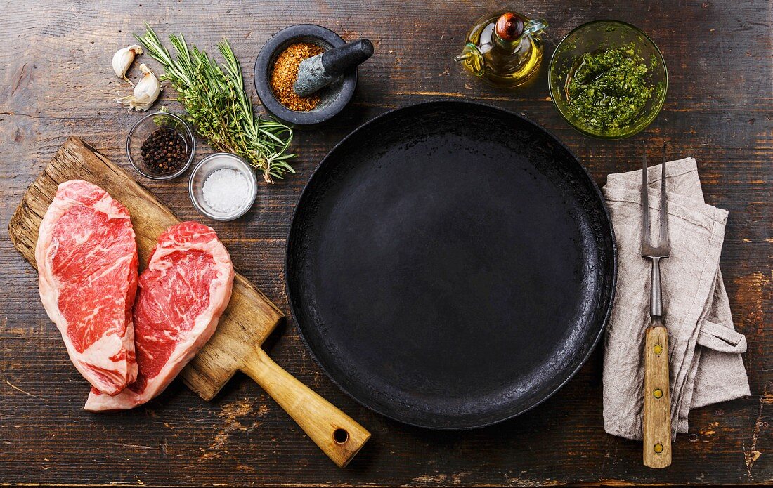 Rohe Striploin Steaks in Herzform, Gewürze und Kräuter um Bratpfanne
