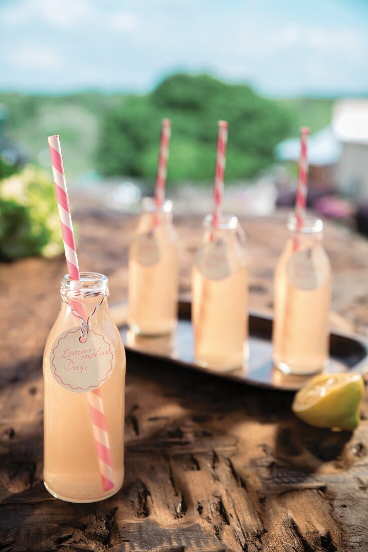 Lemon-Melon-Drop Cocktail in Flaschen mit rosa gestreiften Strohhalmen