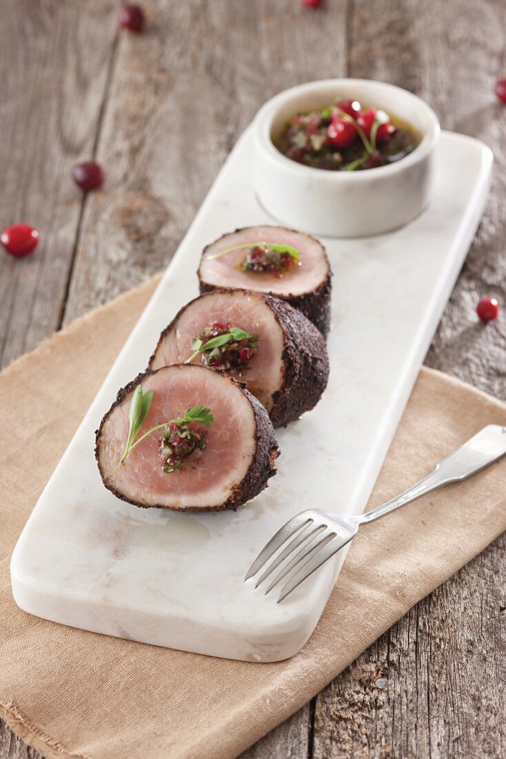 Chili crusted pork tenderloin sliced on white rectanle cutting board with cranberry chimichurri