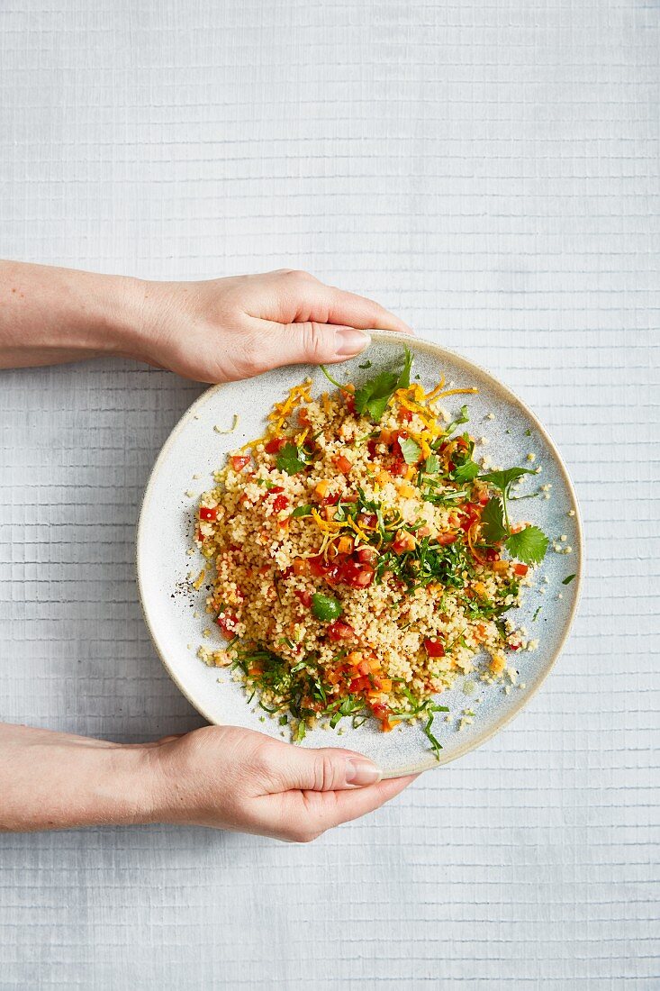Two hands presenting a plate of vegetarian couscous