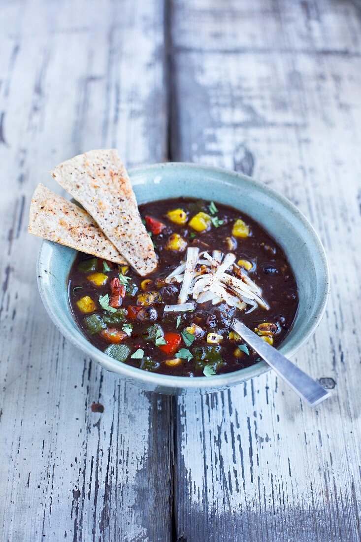 Black bean soup topped with roasted peppers and cilanrto on a rustic white wooden background