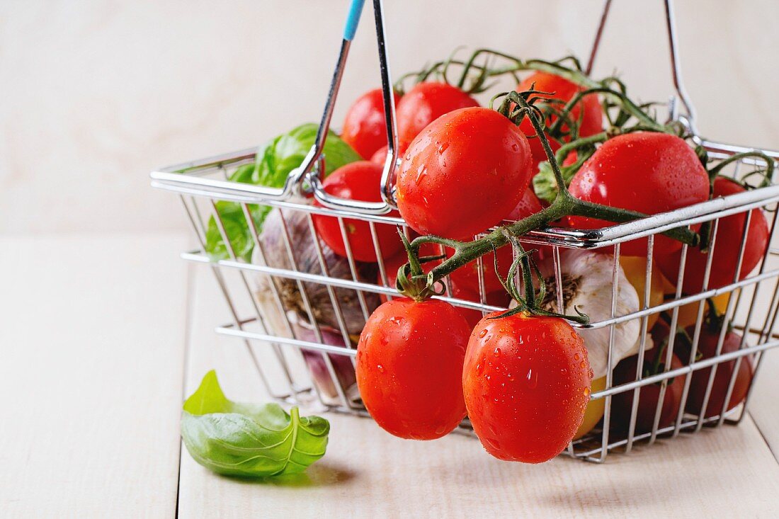 Assortment of cherry tomatoes with garlic and basil in small market food basket over white wooden surface