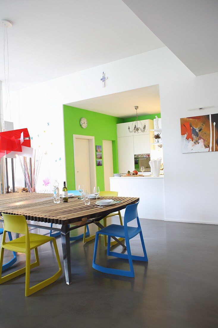 Dining table with blue and yellow chairs in front of open-plan kitchen