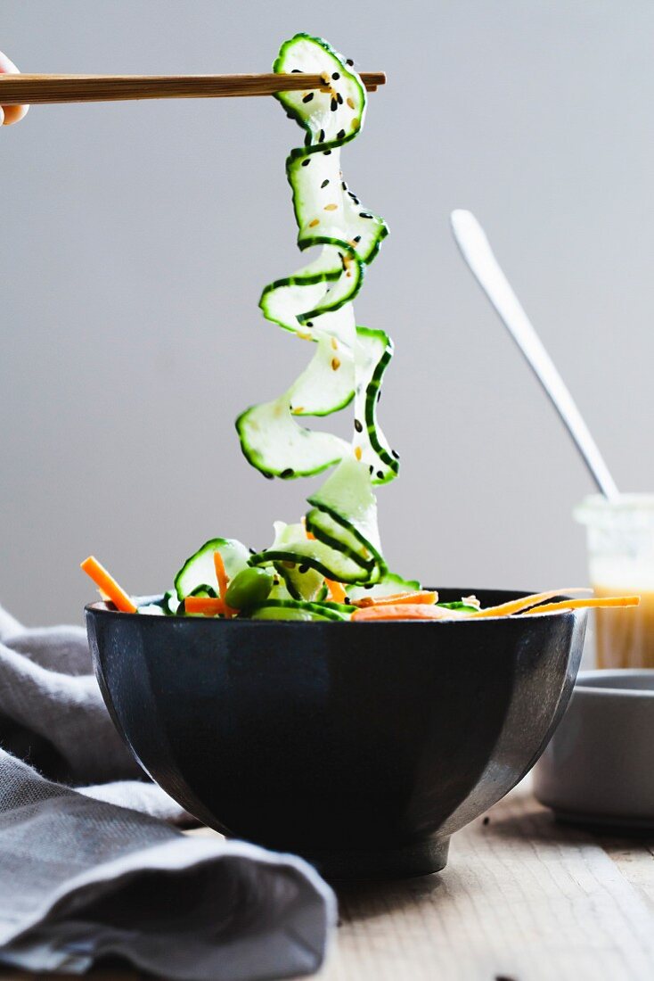 Chopsticks holding spiral cucumber over a salad