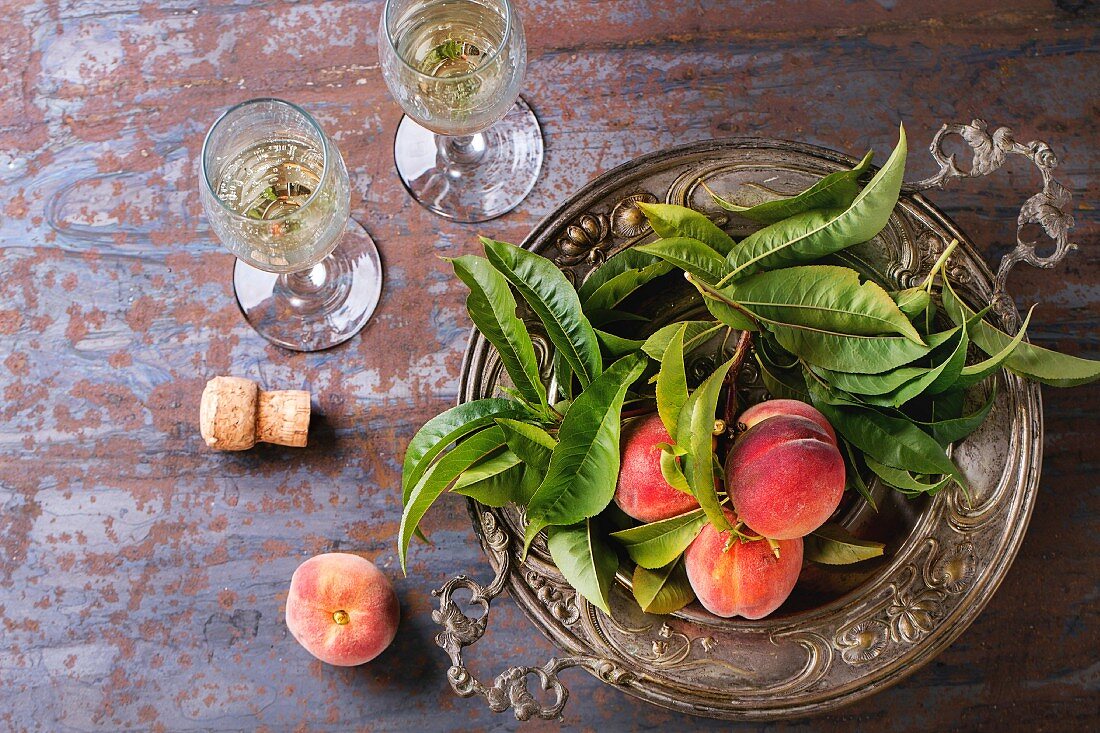 Peaches on branch with leaves in white vintage plate and two glass of champagne with cork over old metal background