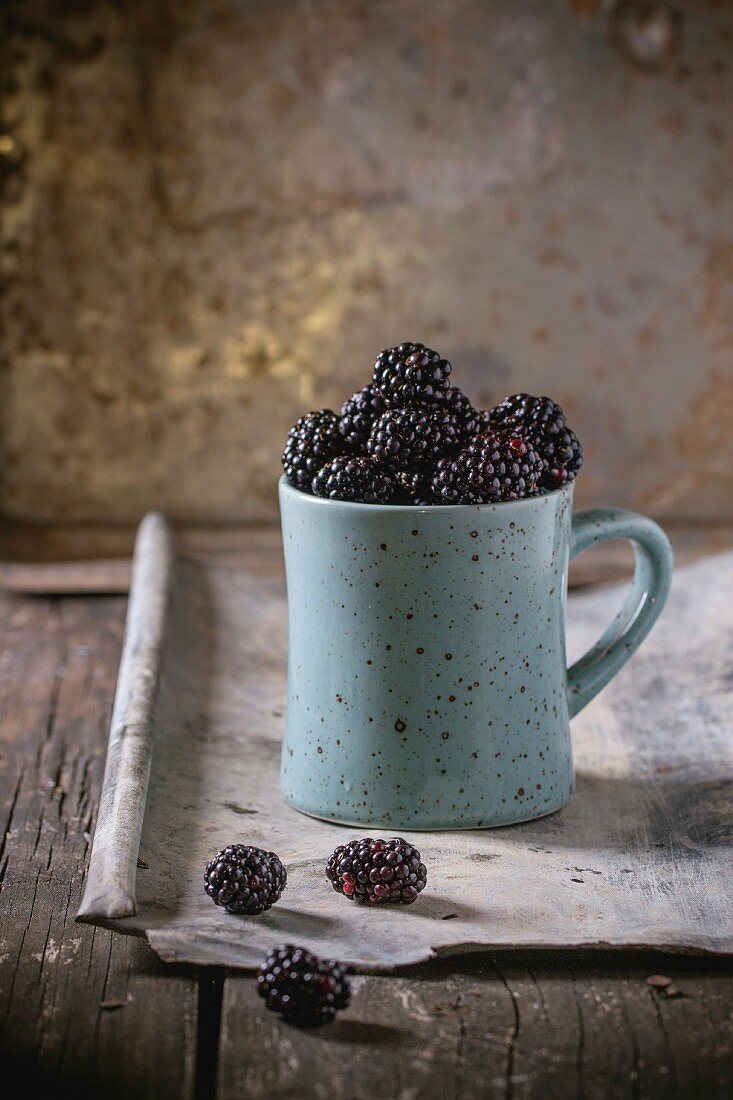 Spotted blue ceramic mug of dewberries, at old wooden table with tin