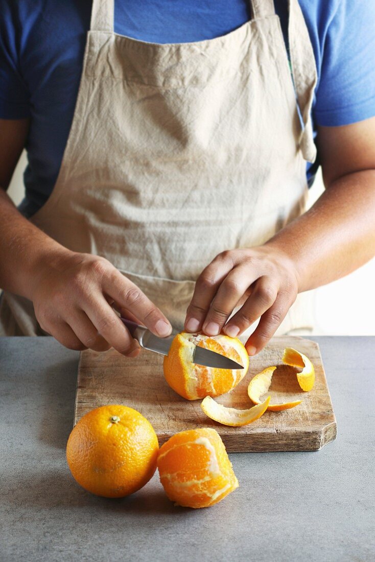 Man peeling an orange with a knife in a kitchen board