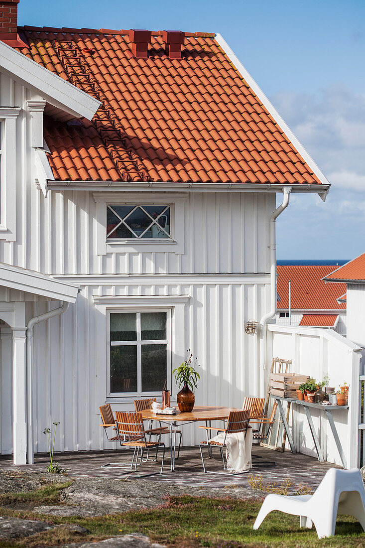 Runder Tisch und Stühle auf der Terrasse vor weißem Holzhaus