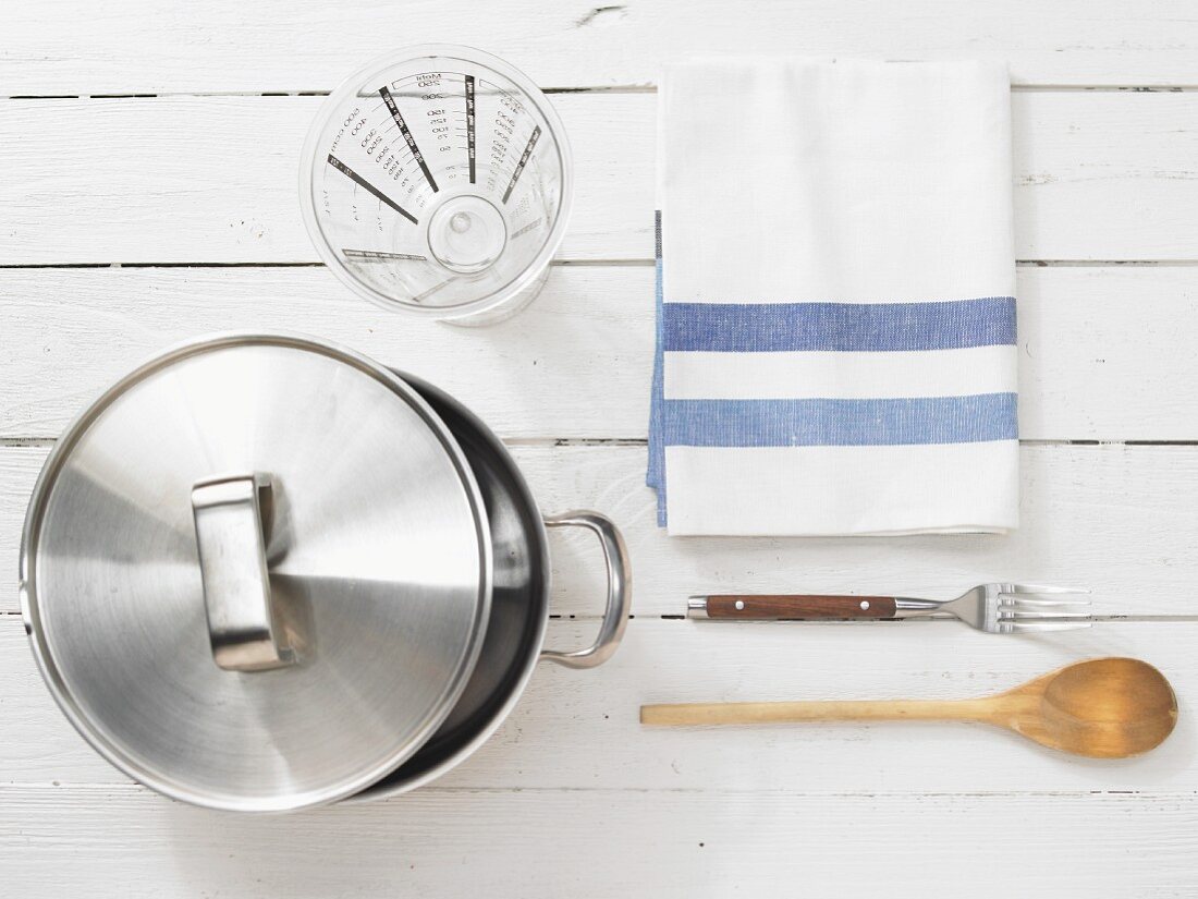 Kitchen utensils: cooking pot, measuring cup, wooden spoon, fork, kitchen towel