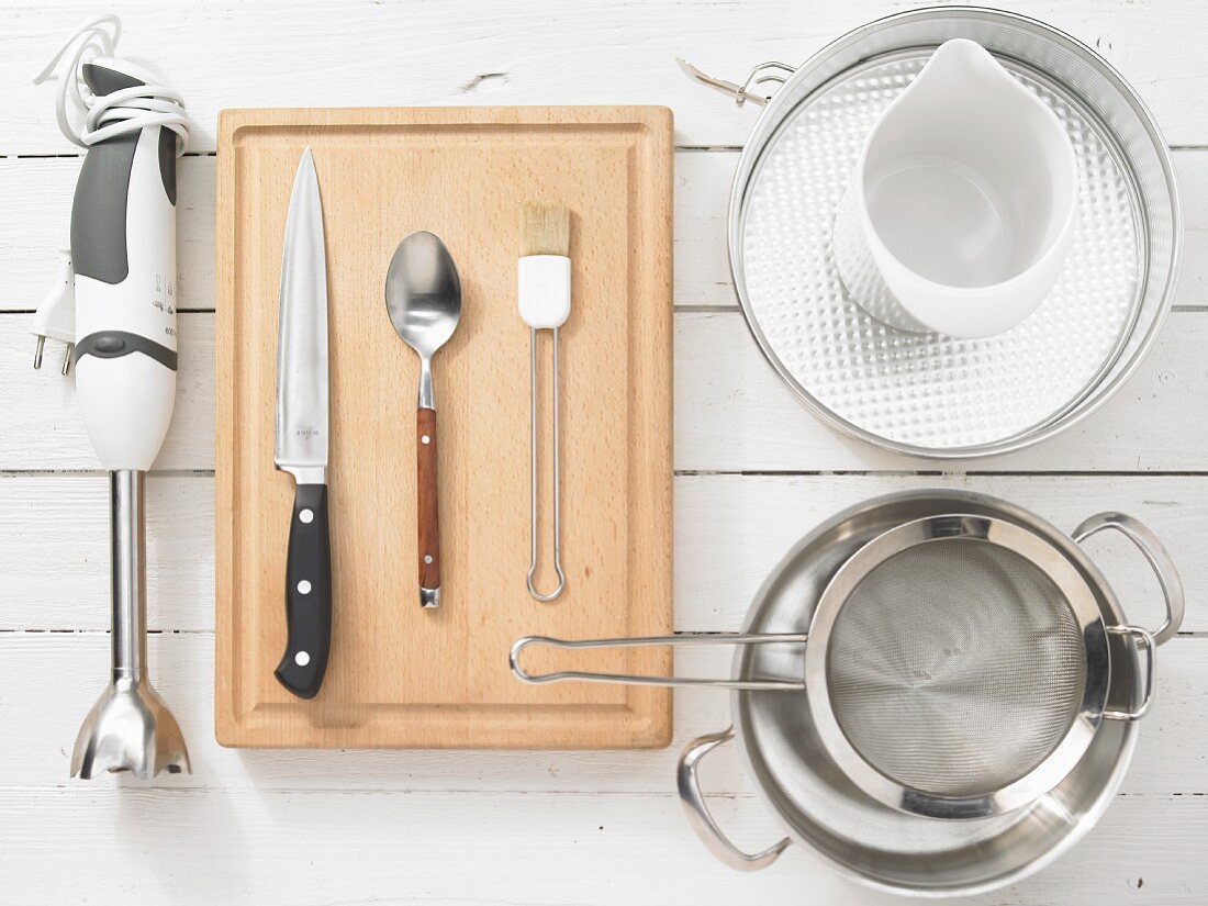 Various kitchen utensils: hand-held blender, cake tin, pot, colander, cutlery, pastry brush