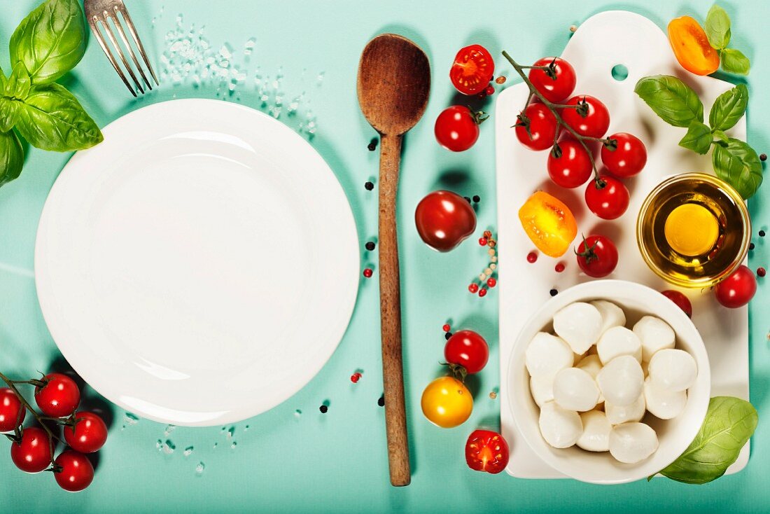 weiße Teller und Zutaten für Caprese-Salat Zutaten auf hellblauem Hintergrund