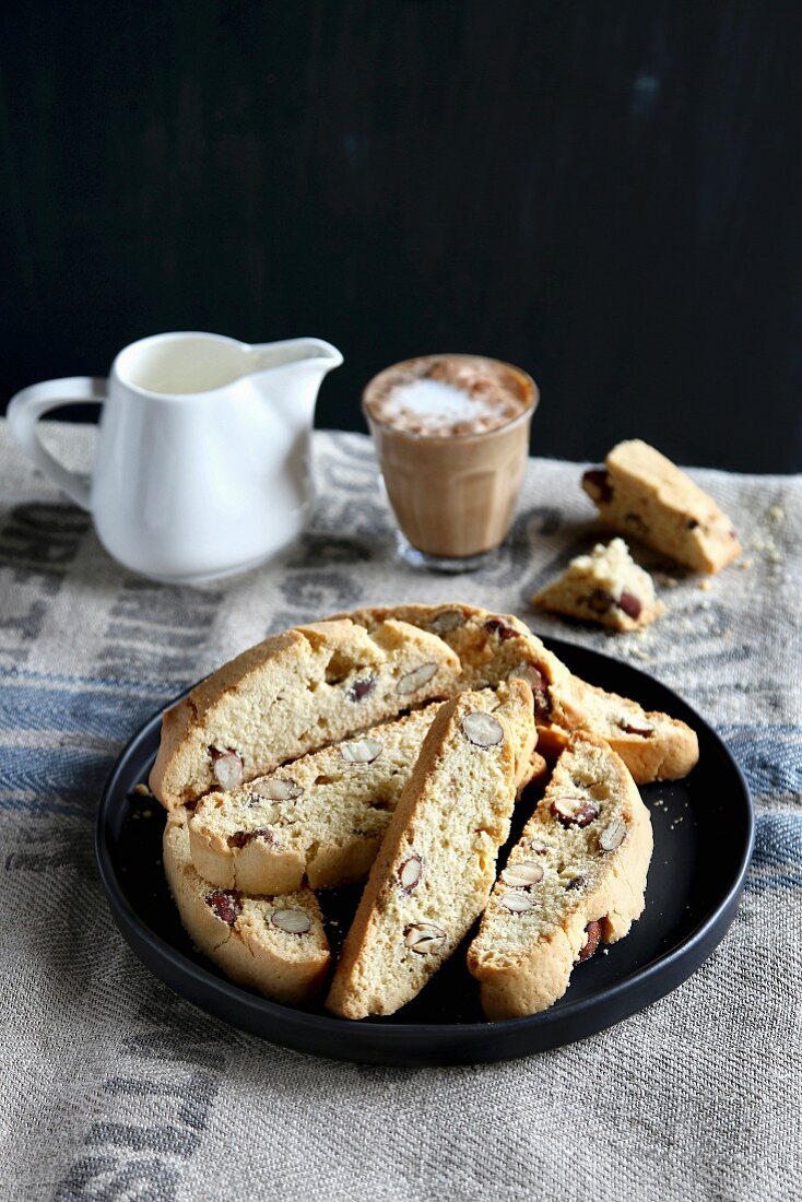 Almond Italian biscotti on a plate with a glass of coffee and a jug of milk in background