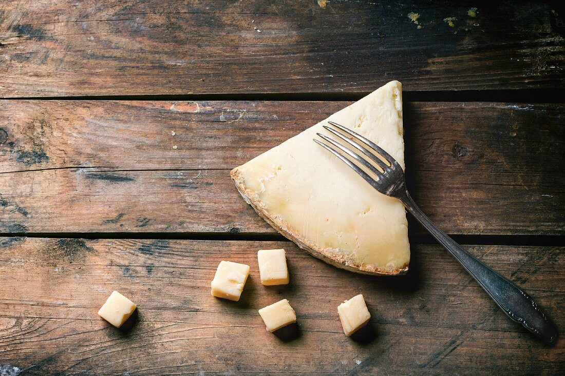 Big piece and little cubes of Belgian cheese with vintage fork over wooden background