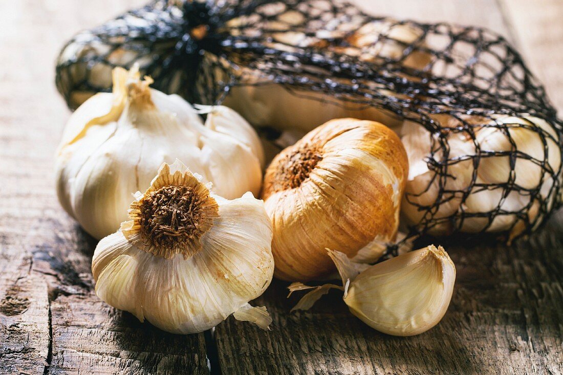 Mesh bag of smoked garlic over wooden background