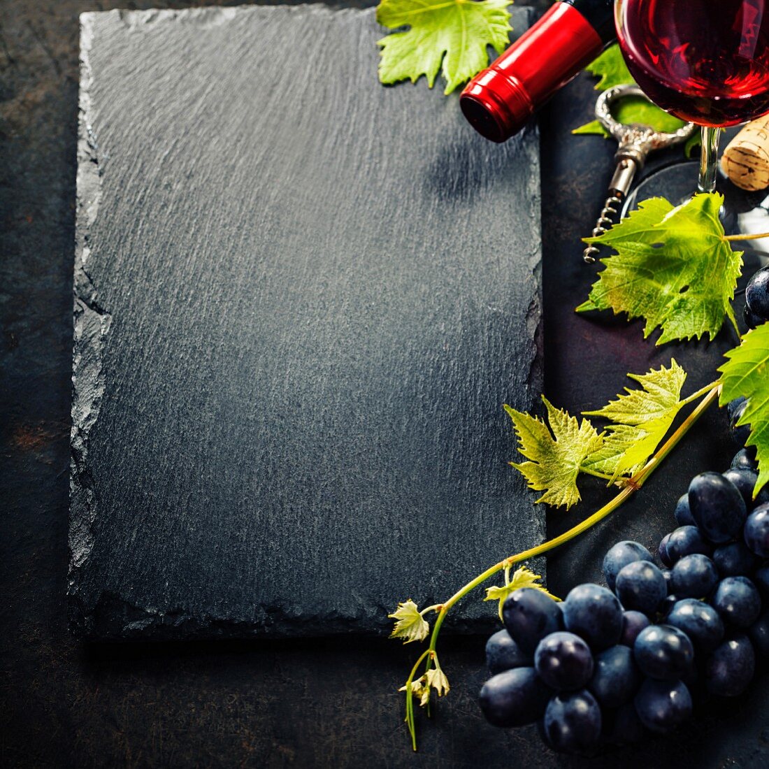 Schieferplatte eingerahmt von Rotwein, Rotweintrauben und Weinranke