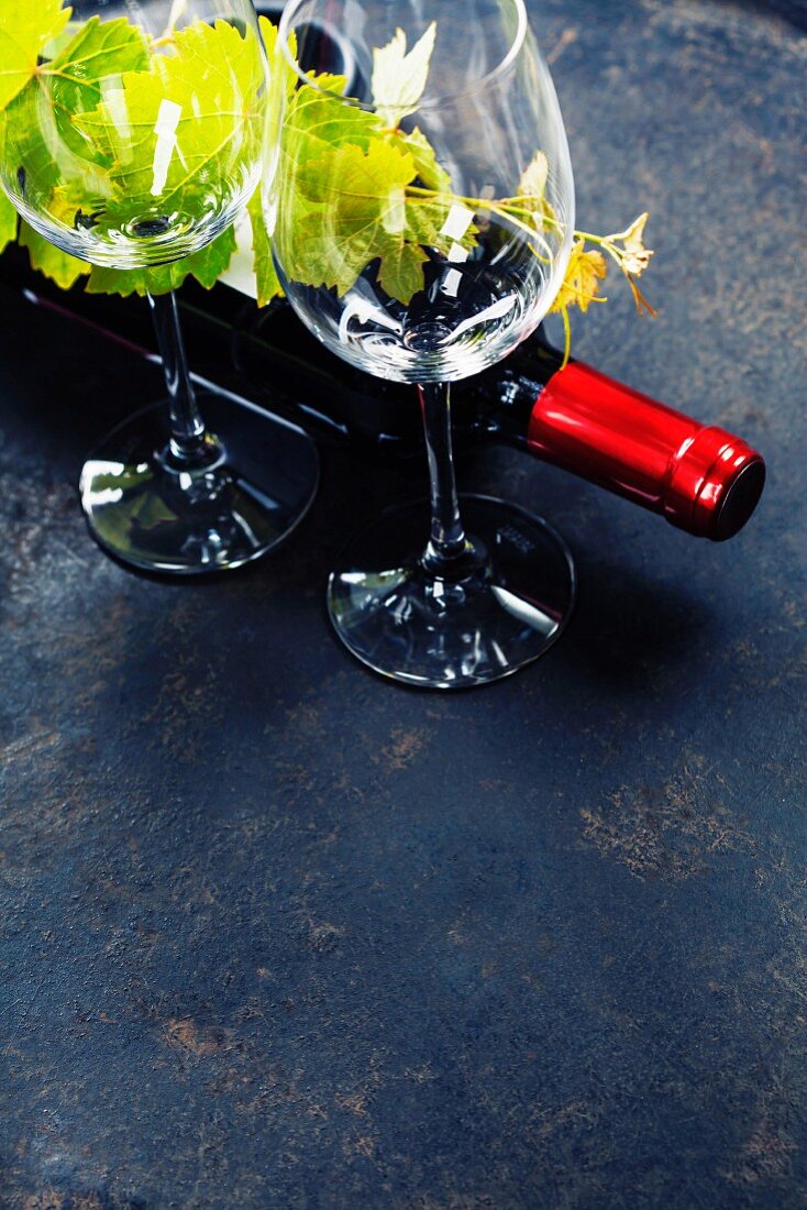 Rotweingläser, Rotweinflasche und Weinblätter auf schwarzem Untergrund