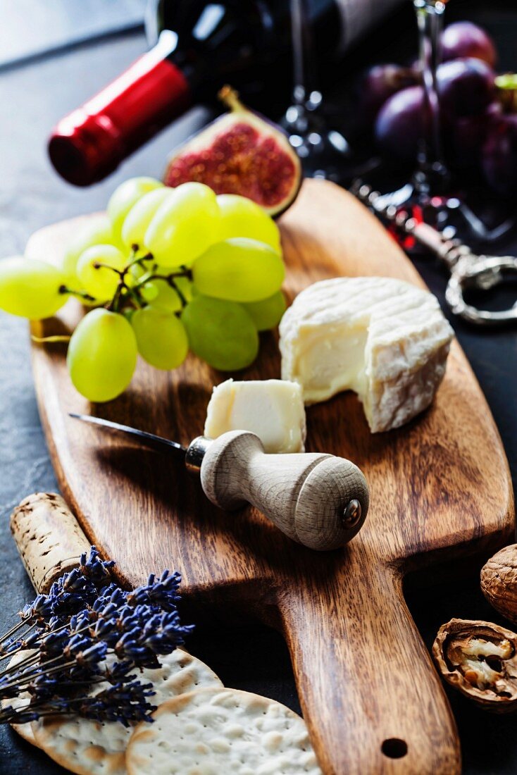 Käse, Trauben und Feige auf Holzbrett, im Hintergrund Rotweinflasche