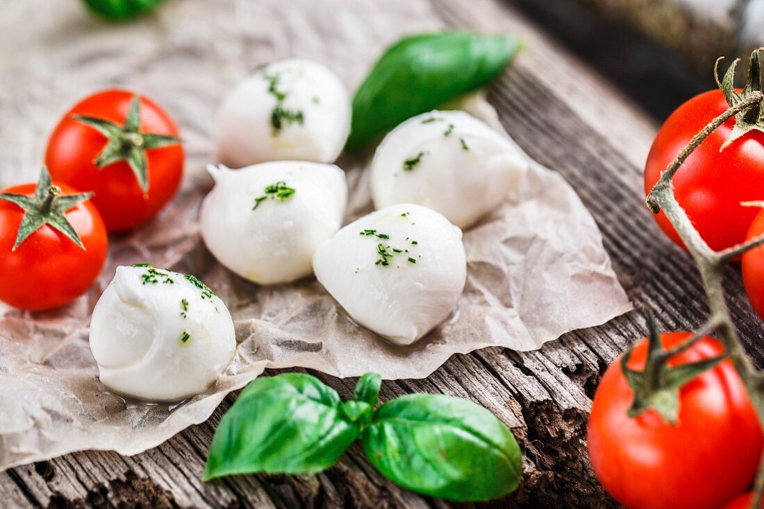 Kirschtomaten, Basilikum und Mini-Mozzarella auf rustikalem Holzuntergrund