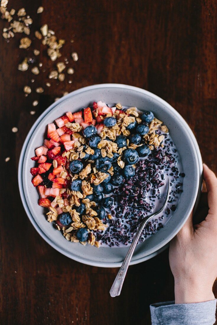 Hand neben Müslischüssel mit schwarzem Reis und Beeren (Aufsicht)