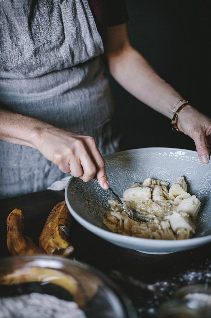 A woman is mashing bananas to be used in a banana bread donut recipe