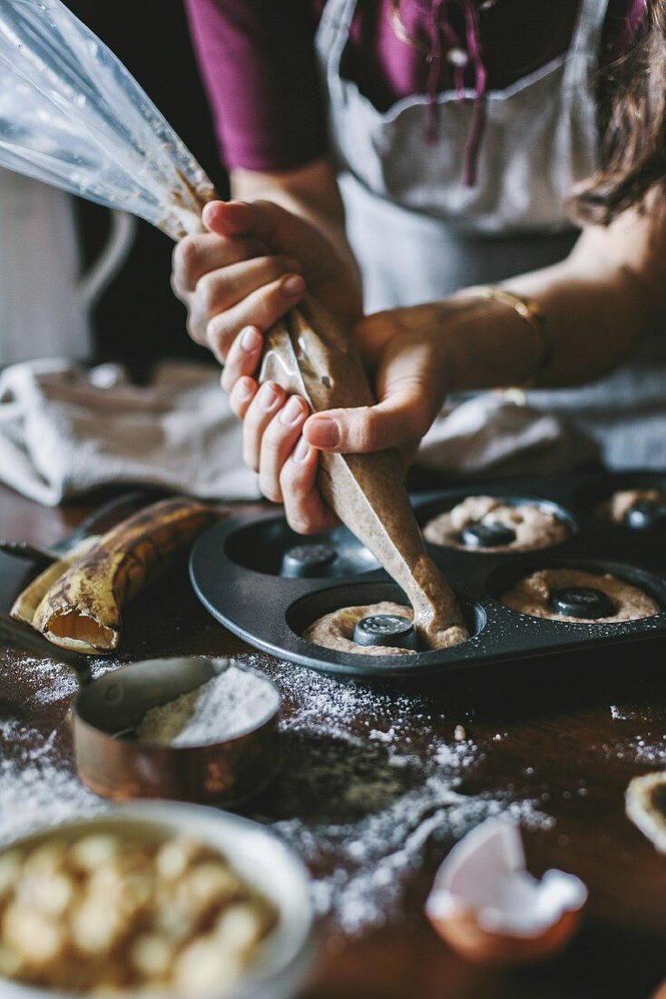 A woman is piping donut batter into donut pan molds