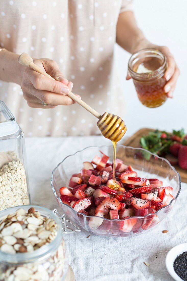 A woman is drizzling a bowl of strawberries and rhubarb with honey