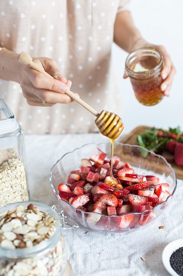 Frau süsst Erdbeeren und Rhabarber in Schüssel mit Honig