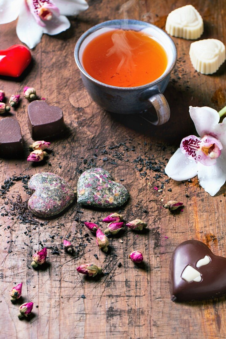 Valentinstag: Pralinen in Herzform zwischen getrockneten Teerosen und Teetasse