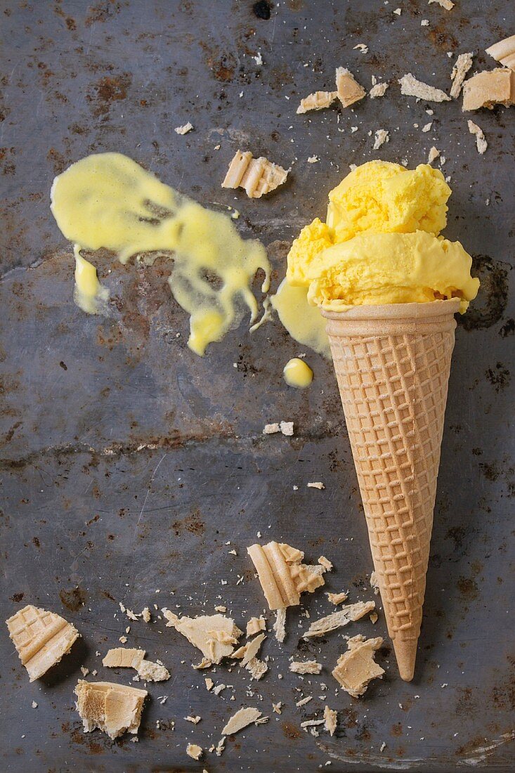Homemade mango ice cream in waffle cone with wafer crumb over rusty metal textured background